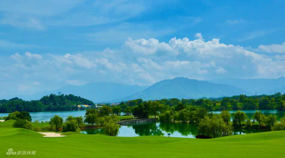 巨大的双层果岭临湖而建，旗杆插在中央，周围环绕着圆形的沙坑，背景是郁郁葱葱的树林。