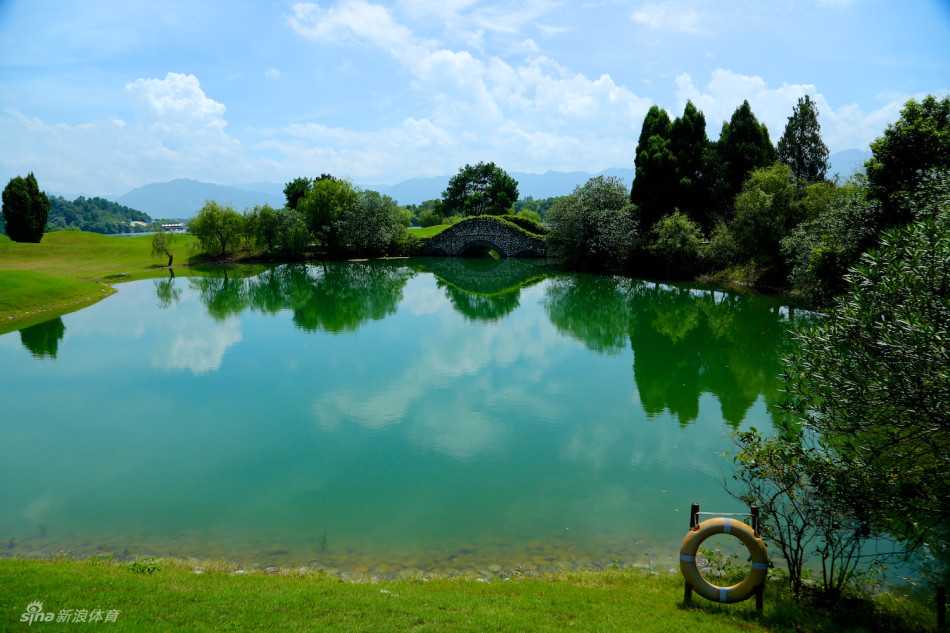 两位球手正在果岭上专注地观察推杆路线，阳光洒在草地上，远处可见湖泊和树木。