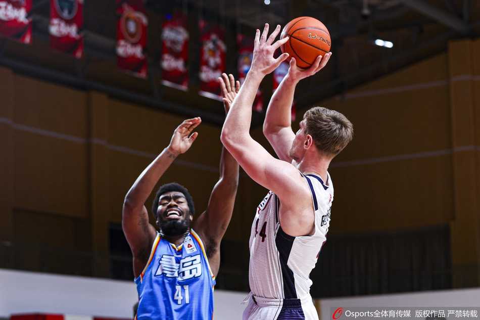 青岛射手赵泰隆出手三分后仍保持完美跟随动作，篮球在空中旋转划过球馆顶部的灯光