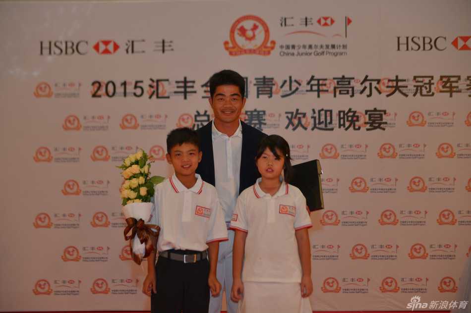 梁文冲与一位小选手并肩合影，他亲切地弯下腰，两人共同举起奖杯，笑容灿烂如阳光。