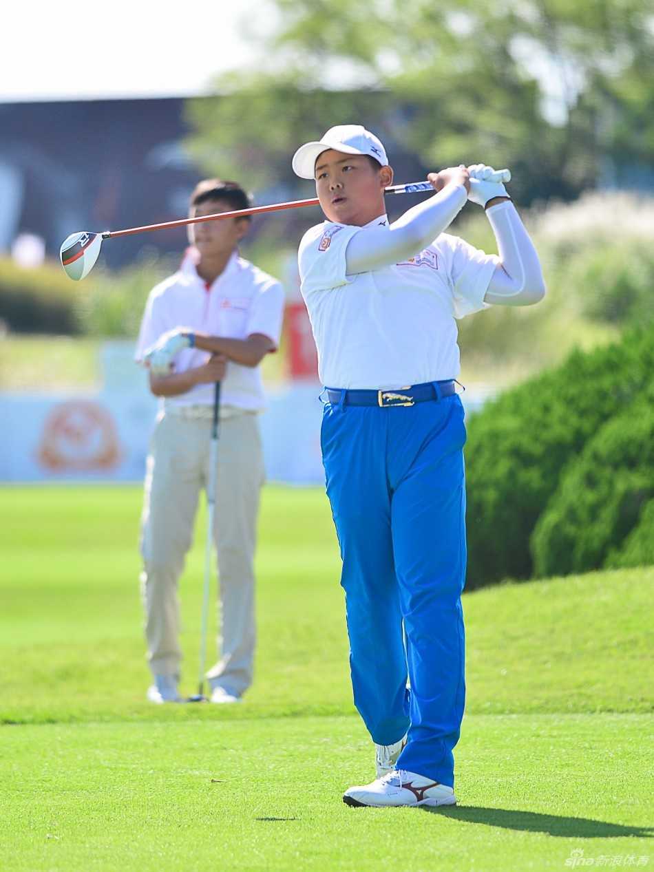 青少年选手冀怡帆正全神贯注地俯身推球，果岭的绿意与她的专注构成一幅动人的画面。