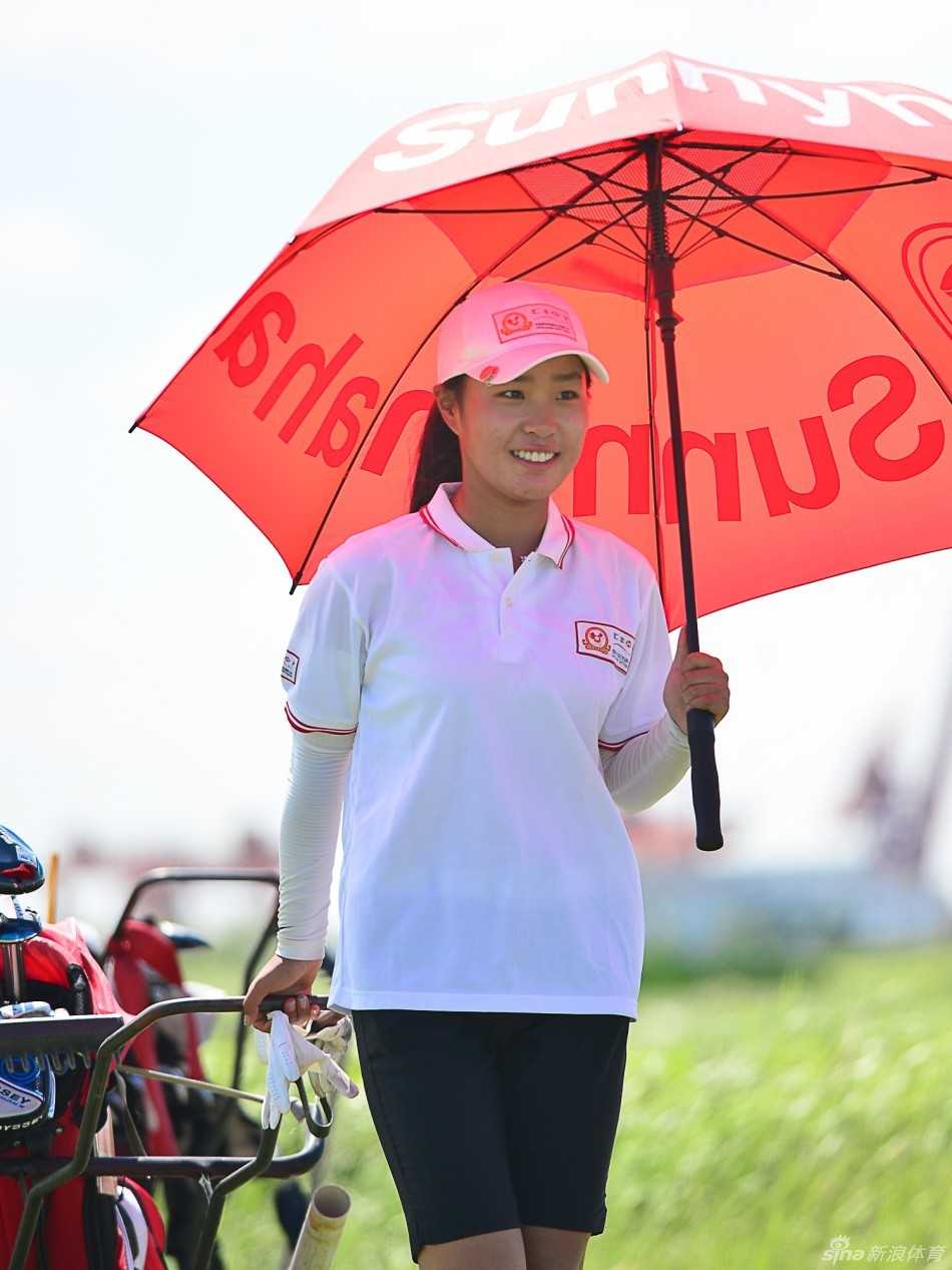 梁文冲在绿草如茵的练习果岭旁，亲自示范推杆动作，小选手们在旁认真观摩学习。