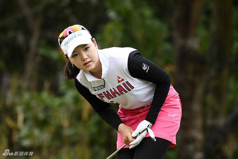 韩国选手申智爱在果岭旁执旗凝神，旗帜在风中微扬，她的眼神中闪烁着计算与决断的光芒