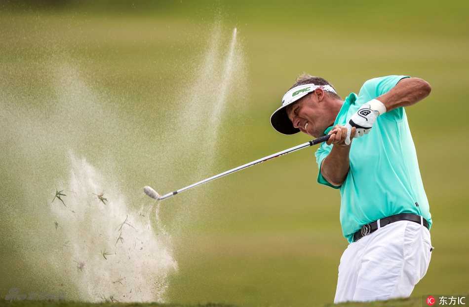 雅各布森在及膝的长草中站稳脚跟，全力挥杆试图将小球救出，激起一片草屑，画面充满了力量与挣扎感。